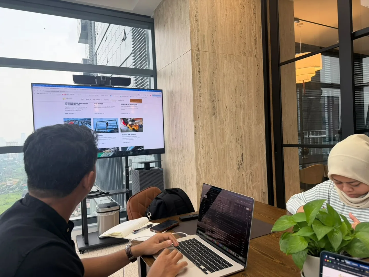 Aqil Zikry in a meeting with clients, reviewing a website on the wall screen with laptops open on the table